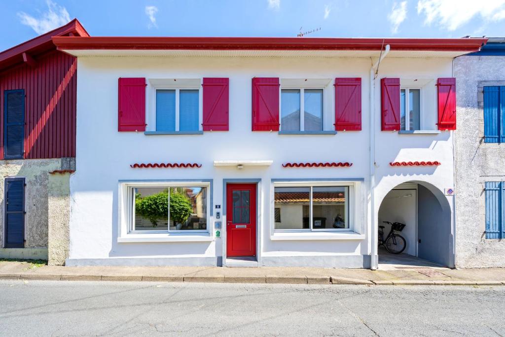 a white house with red shutters and a red door at Chambres D'hôtes Madan'hôte in Capbreton