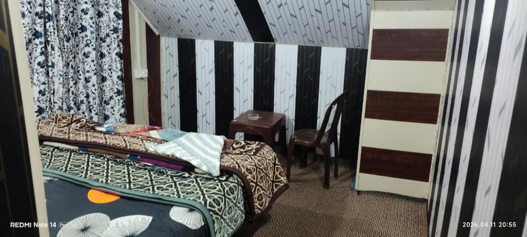 a small bedroom with a bed and a chair at BAKSHI lodge in Pahalgām