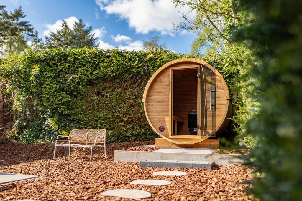 a circular wooden sauna with a chair in a garden at Luxe wellnesshuis op de Veluwe in Lunteren