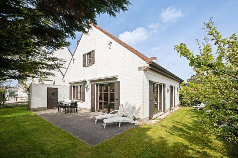a white house with a patio and a table and chairs at Bretoenselaan 5 in De Haan