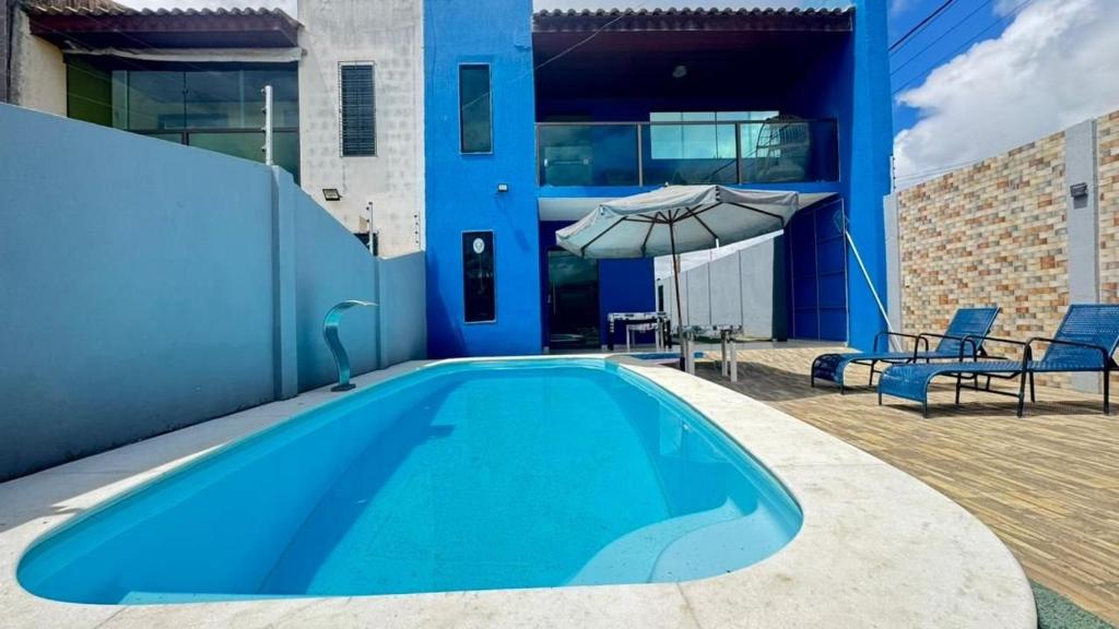a blue swimming pool with a patio and an umbrella at Casa em Gravatá com piscina privativa por Yolo in Gravatá