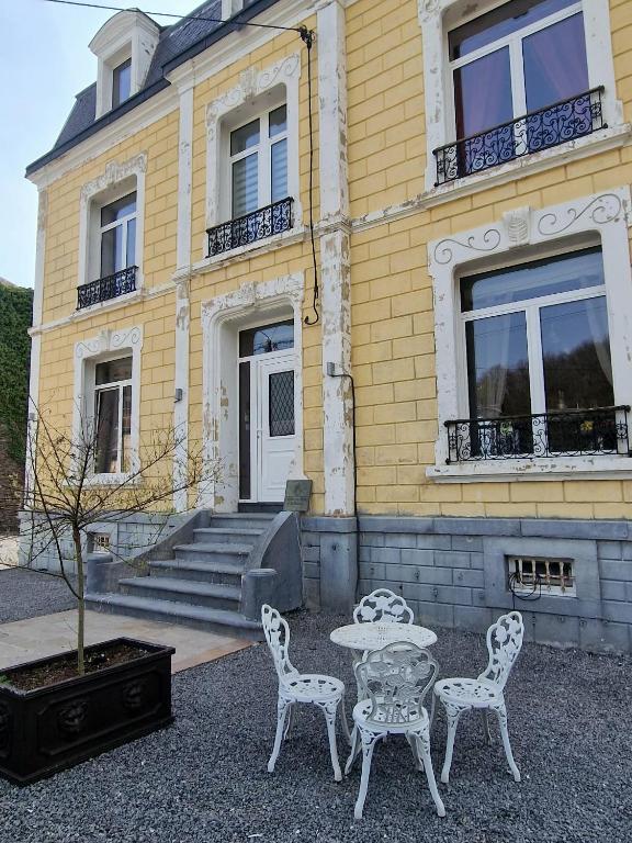 a table and chairs in front of a yellow building at Le Reflet de la Semoy in Les Hautes-Rivières