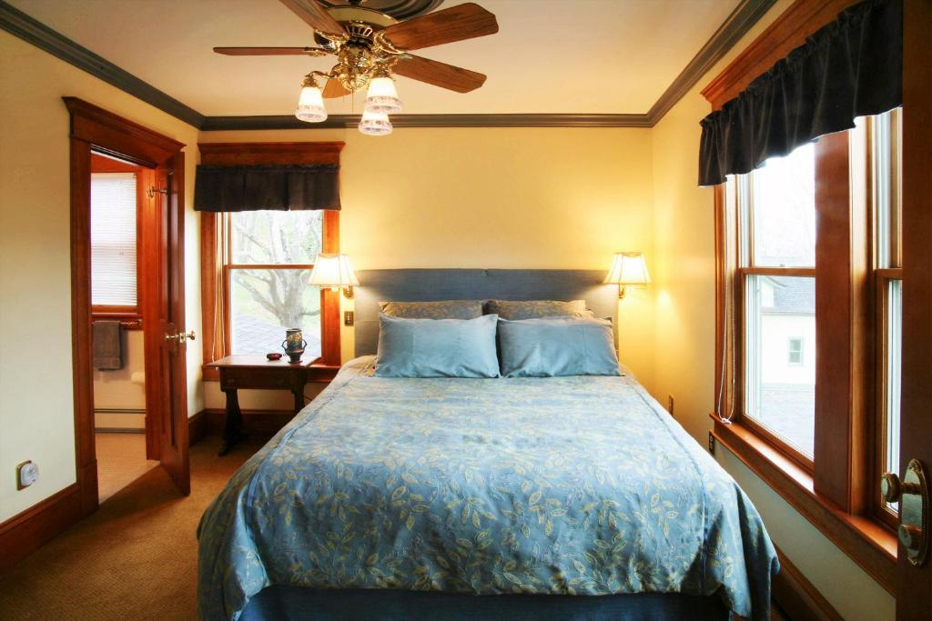 een slaapkamer met een bed met een blauw dekbed en 2 ramen bij Breezy Hill Inn in Fleischmanns
