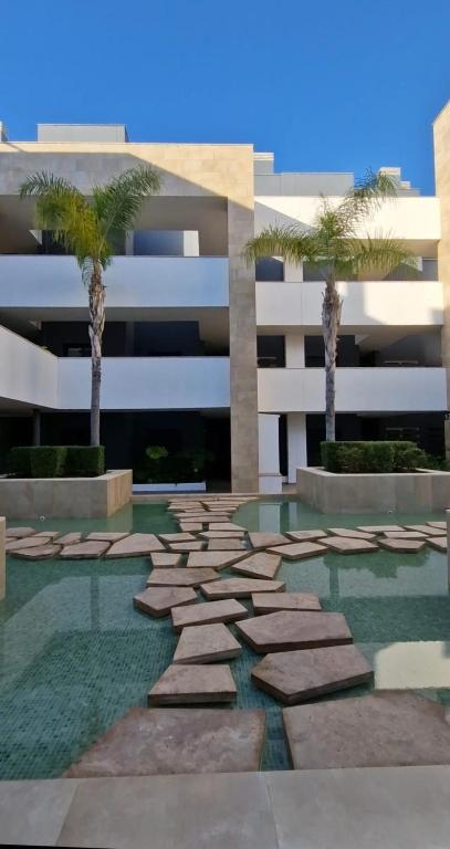 a building with two palm trees and a stone pathway at Flamenca Village Apartment SALSA in Orihuela Costa