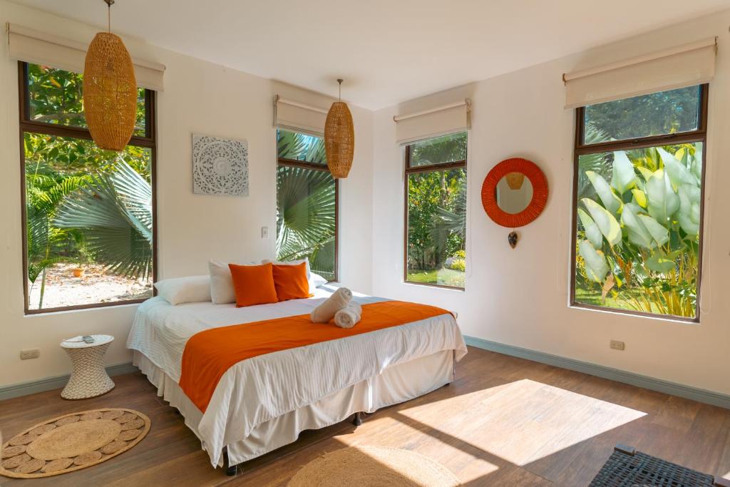 a bedroom with a bed with orange sheets and windows at Selvática Residences in Puerto Viejo