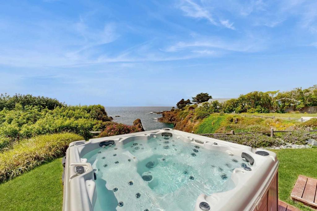 a hot tub in the grass next to the ocean at Luxe Remodeled Oceanfront Home on the Bluff in Mendocino