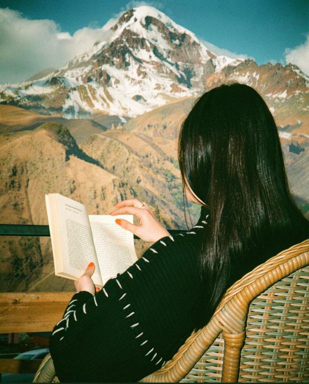 a woman reading a book in front of a mountain at Lonely Mountain in Kazbegi