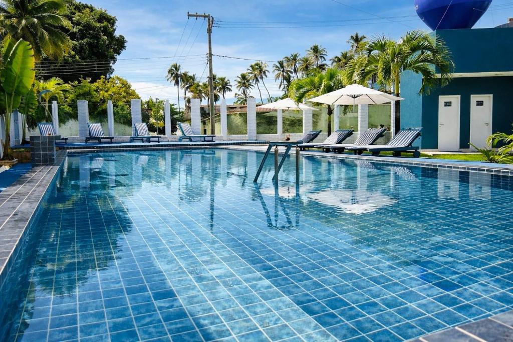a swimming pool with chairs and trees and a building at Hotel Summer Beach Paripueira Maceió in Paripueira