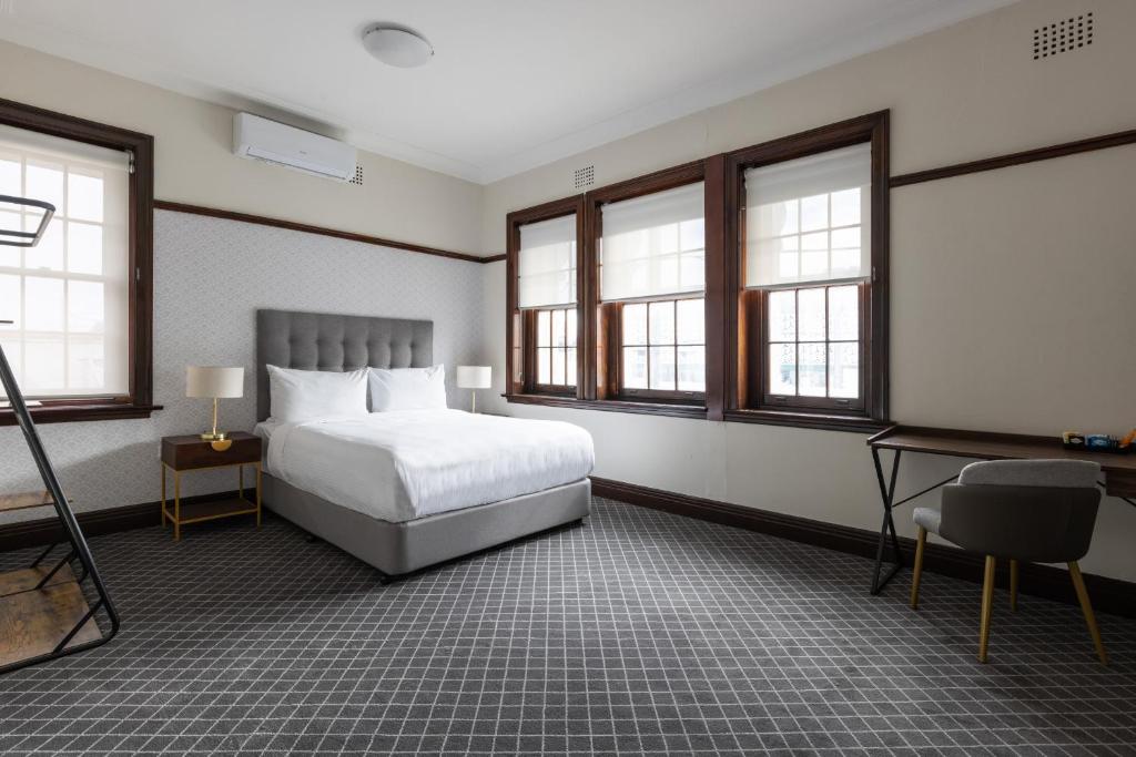 a bedroom with a bed and a desk and windows at Southern Cross Hotel in Sydney