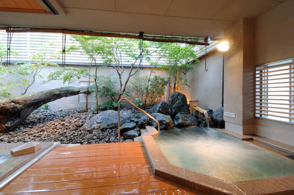 a hot tub in a room with trees and rocks at Kanazawa Manten Hotel Ekimae in Kanazawa
