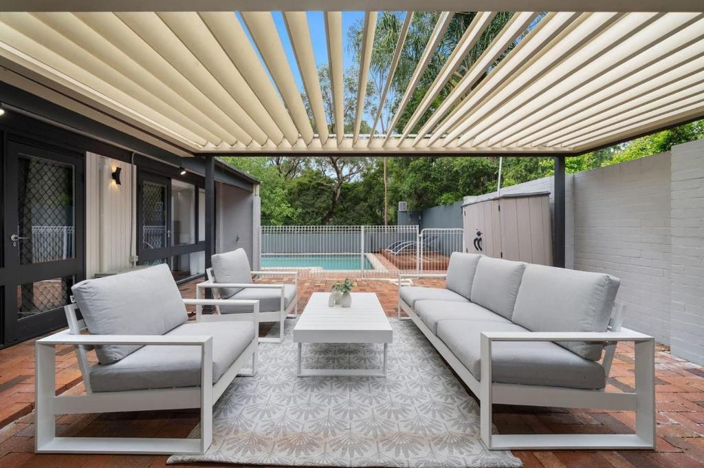 a patio with white couches and a table at Tranquil bush resort house - pool & fire pit in Pymble