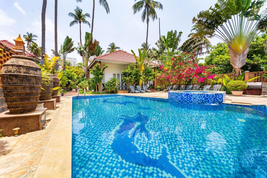 a swimming pool in front of a house with palm trees at Sunday Lotus Garden Resort By The Sea Mui Ne in Mui Ne