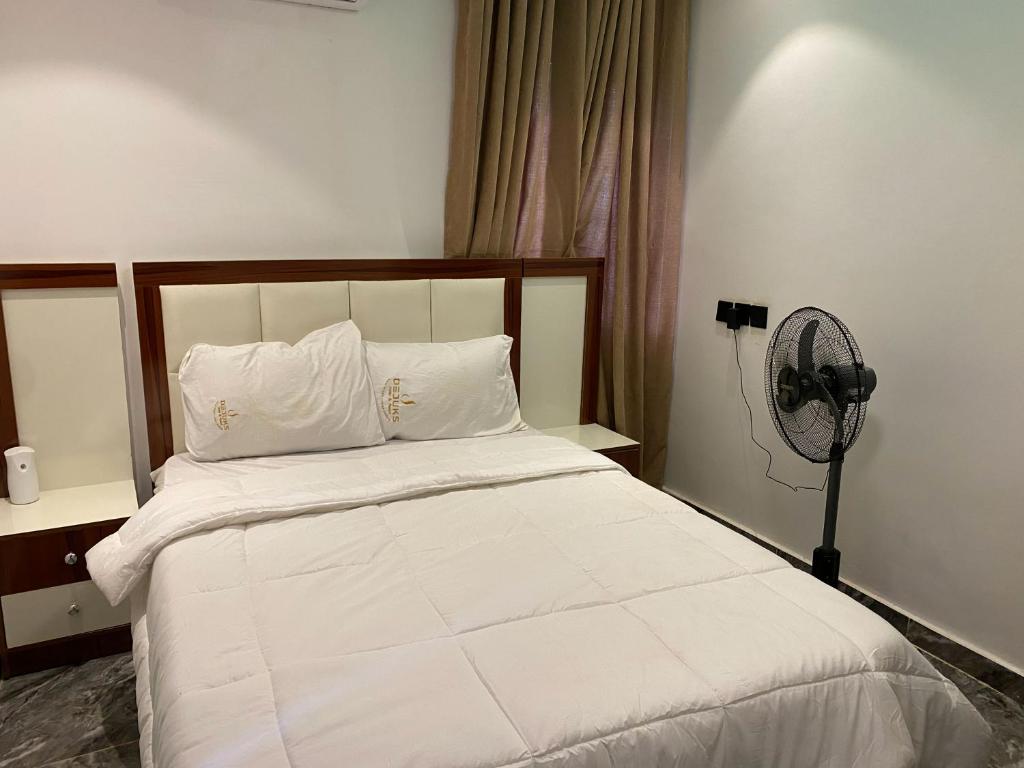 a bedroom with a bed with white sheets and a fan at Dejuks Hotel & Resort in Akure