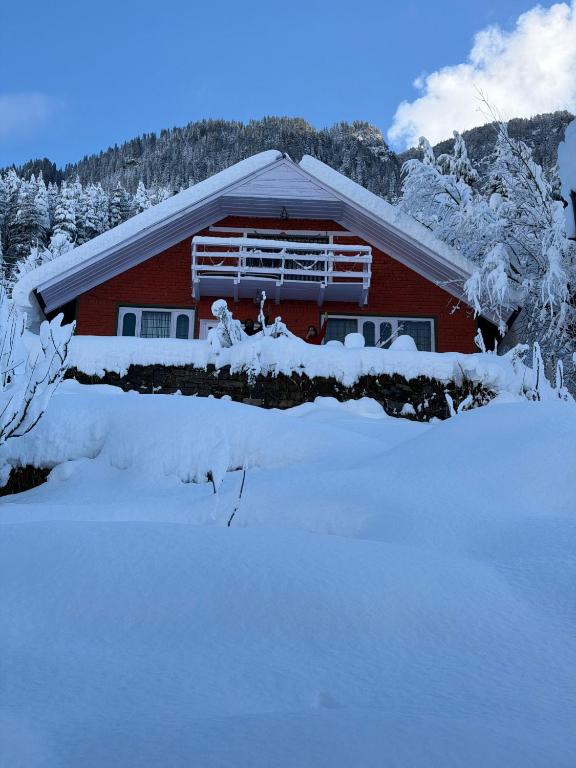 a red house with snow on the ground in front of it at Mistvale Cottage in Manāli