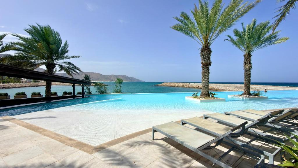 ein Swimmingpool mit zwei Palmen und Stühlen in der Unterkunft Ocean crescent by Bait Zain in As Sīfah