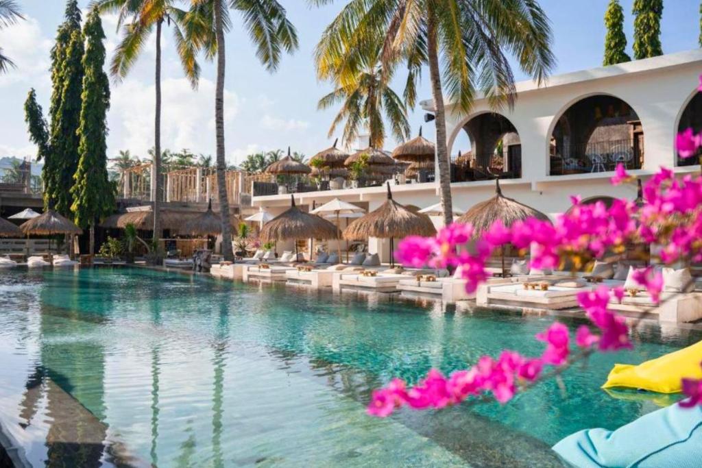 a pool at a resort with palm trees and pink flowers at Dwayne 1 BR Standard Room in Kuta Lombok
