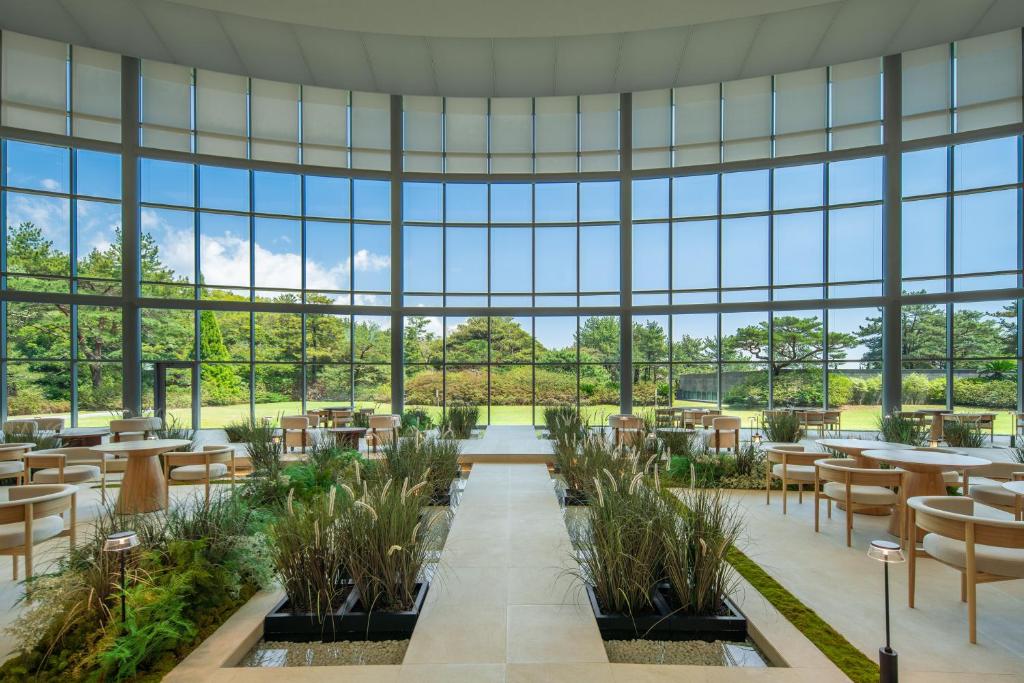 ein Restaurant mit Tischen und Stühlen und großen Fenstern in der Unterkunft WE Hotel Jeju in Seogwipo