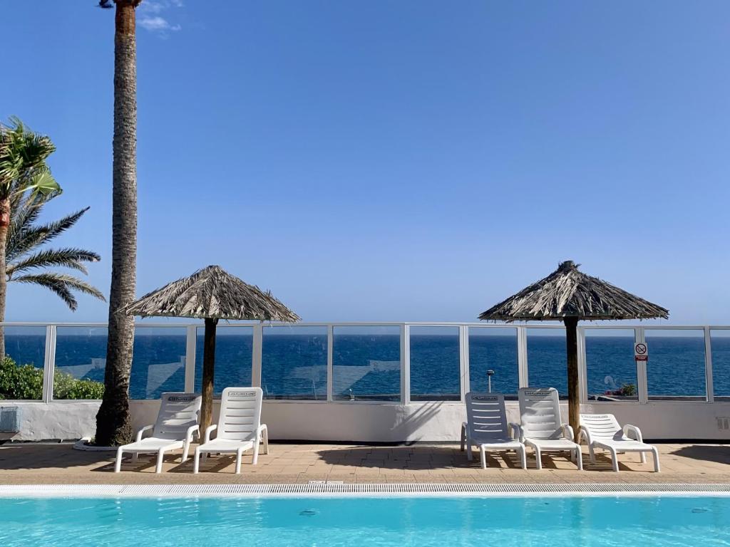 a group of chairs and umbrellas next to a swimming pool at Bungalow Atlantic View in Maspalomas