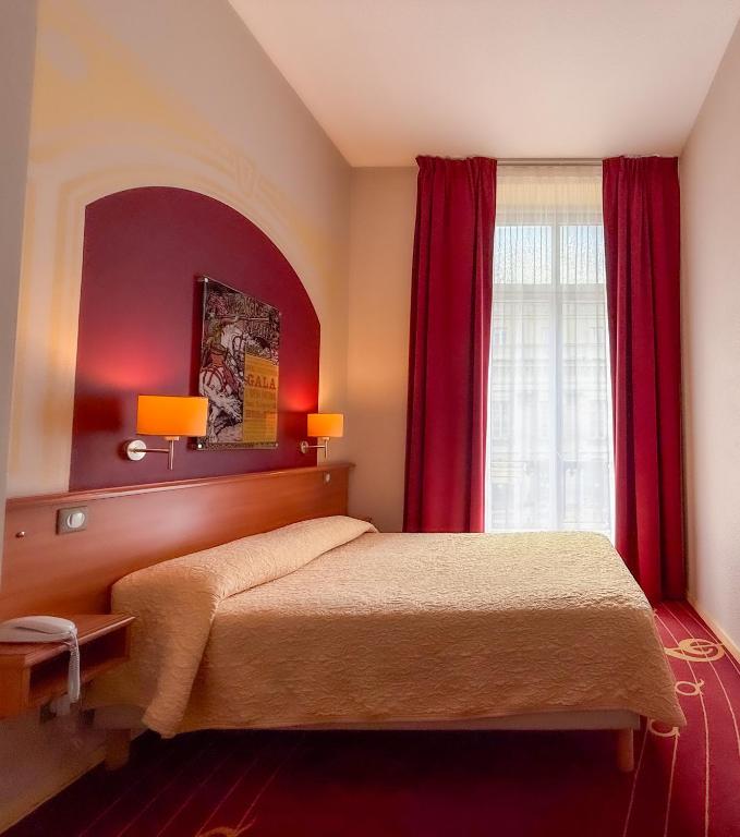 a bedroom with a bed with red curtains and a window at Hotel de L'Opéra in Bordeaux