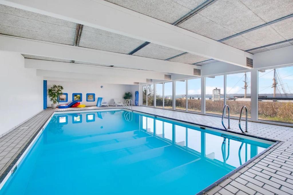 a swimming pool with blue water in a building with windows at Vigen ferielejligheder in Ebeltoft