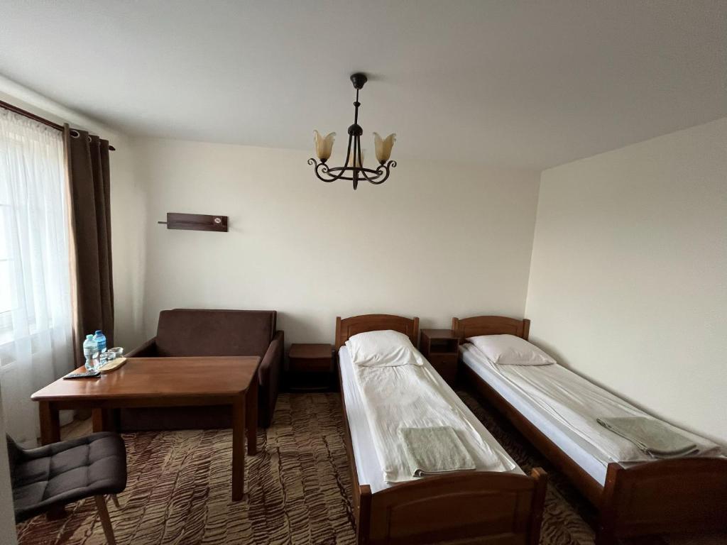 a room with two beds and a table and a chandelier at Hotel Lanckorona in Jędrzejów
