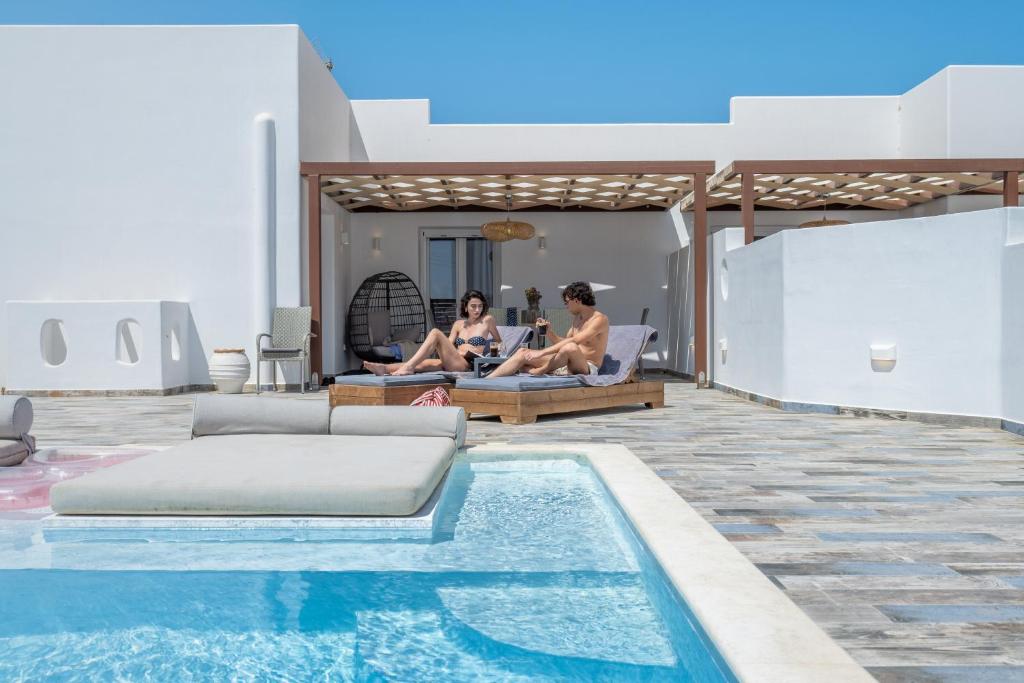 two people sitting on lounge chairs next to a swimming pool at Depis luxury private villas in Plaka