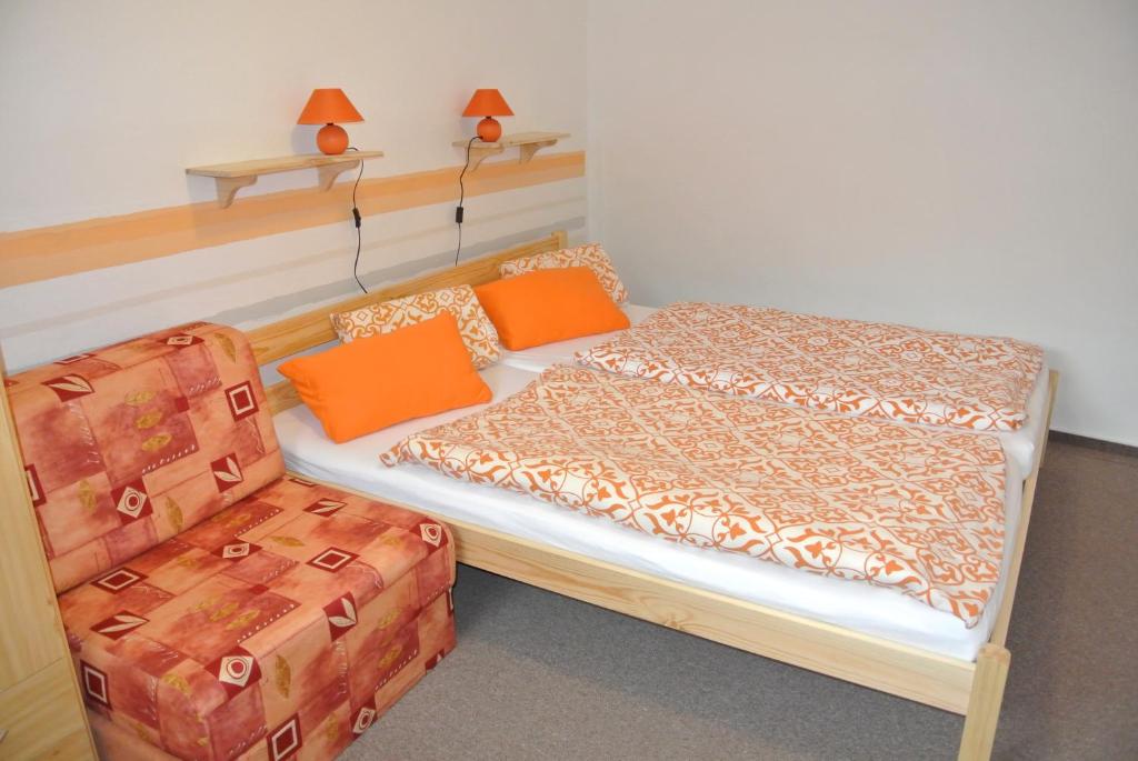 1 dormitorio con 1 cama y 1 silla con almohadas de color naranja en Apartmány Růže, en Lipová-lázně
