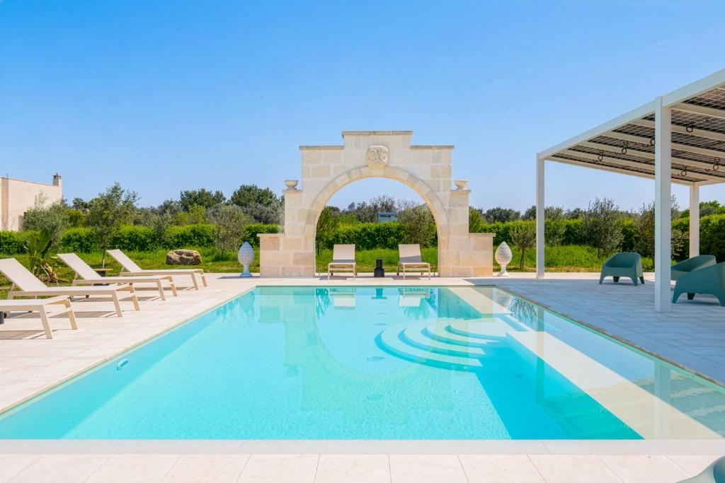 a swimming pool with chairs and an arch in the background at Villa Kalia Luxury by HDSalento in Aradeo
