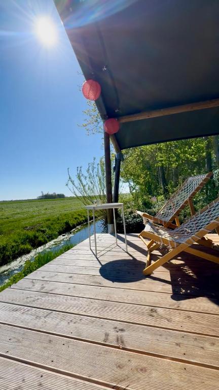 a wooden deck with two chairs and a boat at Glamping Safaritent 4 persoons in Hindeloopen