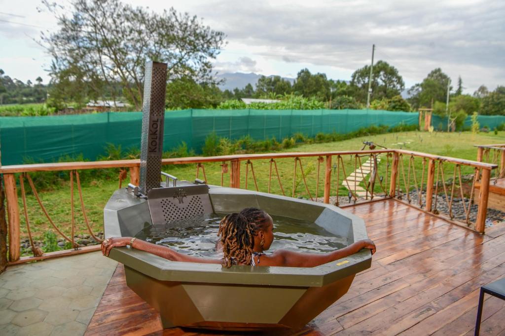 a woman laying in a bath tub on a deck at 2BR Forest Cabin, Jacuzzi, Fireplace & Mt Kenya Views in Naro Moru
