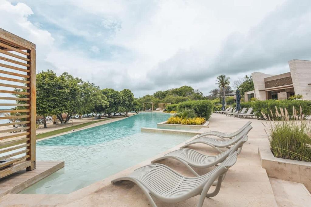 a swimming pool with three white chairs in a park at Oceanview 3br condo w spa & gym u603 in Barú