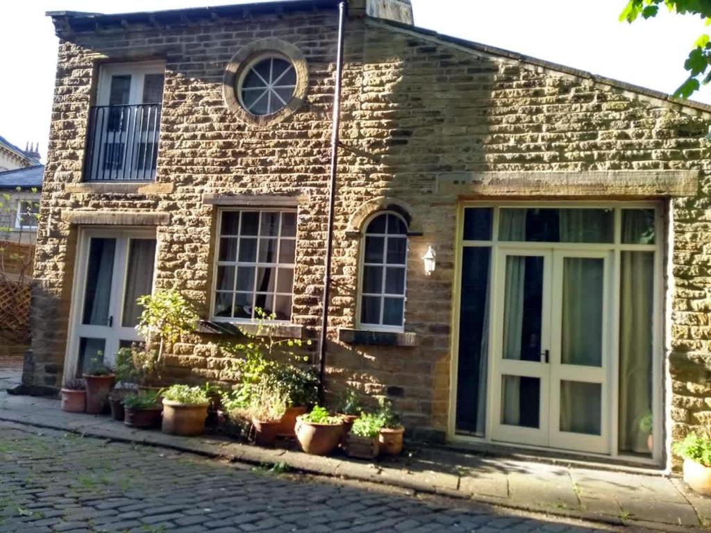 a brick house with potted plants in front of it at Edgerton cottage, large 1-bed detached coach house in town, Spacious rustic charm in Lindley