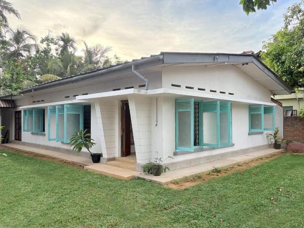 a white house with blue windows and a yard at Achcha's Place in Negombo
