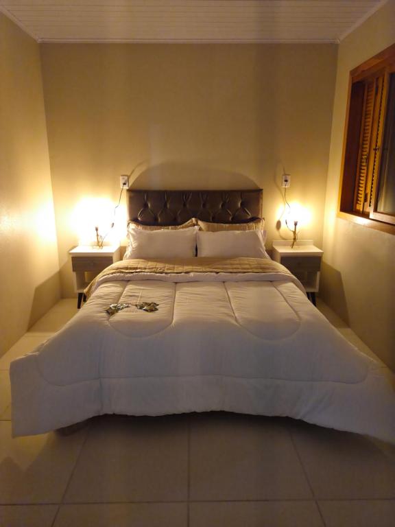 a large white bed in a bedroom with two tables at Casa com dois quartos cama de casal e vista panorâmica próximo a Gramado Serra Gaúcha in Igrejinha