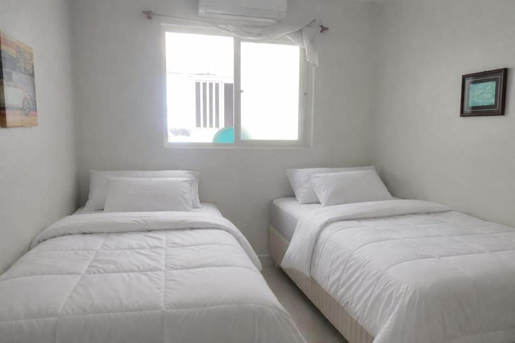 two beds in a white room with a window at Casa XV de novembro em Garanhuns in Garanhuns