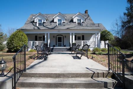 a white house with chairs in front of it at Swamp Rabbit Inn TR in Travelers Rest
