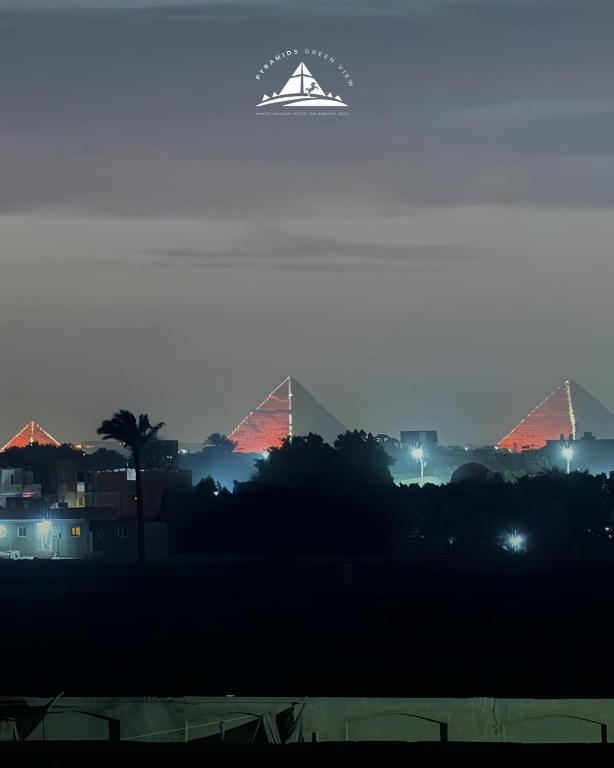 a view of the pyramids of giza at night with a white logo at Pyramids Green View in Cairo