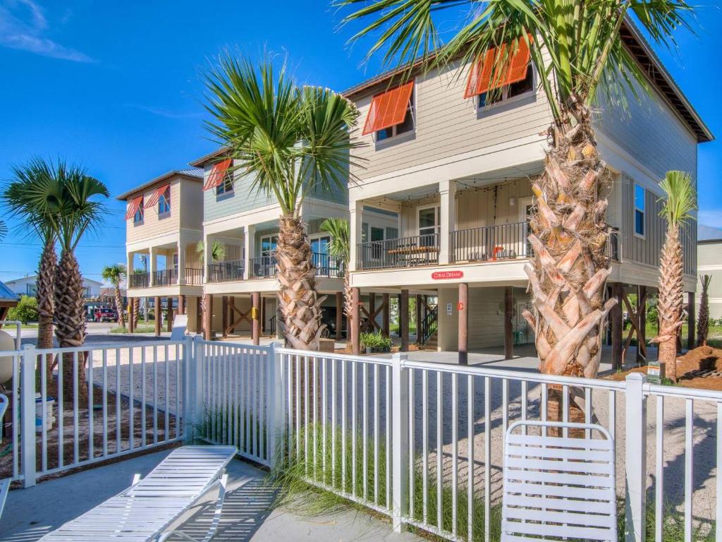 a white fence in front of a building with palm trees at PRIME Coral Dreams Walk to Beach Pool Pets Near The Hangout Parking in Gulf Shores