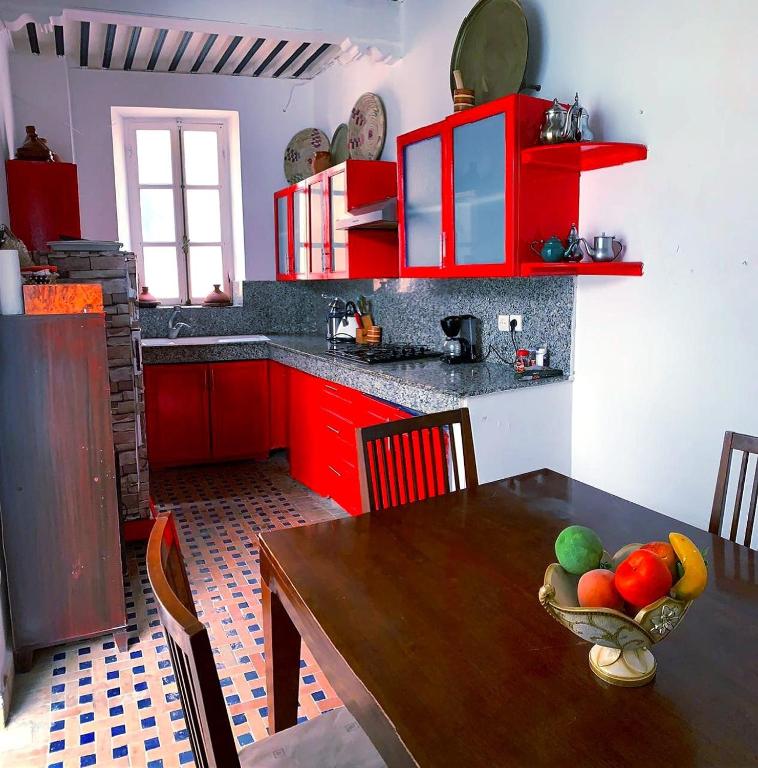 a kitchen with red cabinets and a wooden table with a bowl of fruit at Dar darkom in Essaouira