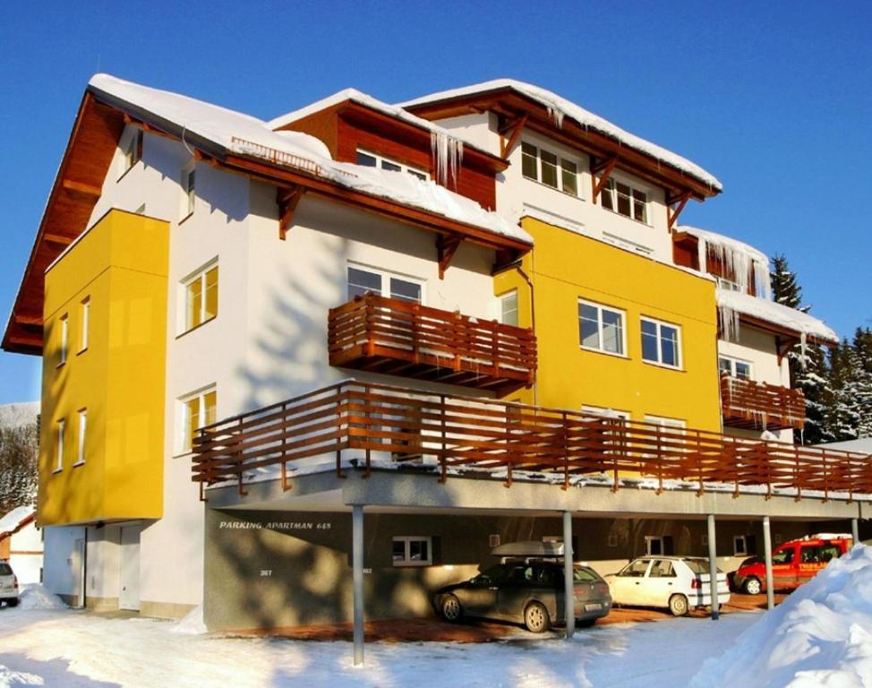 ein gelbes und weißes Gebäude mit Autos im Schnee in der Unterkunft Apartmán Karolína Harrachov in Harrachov