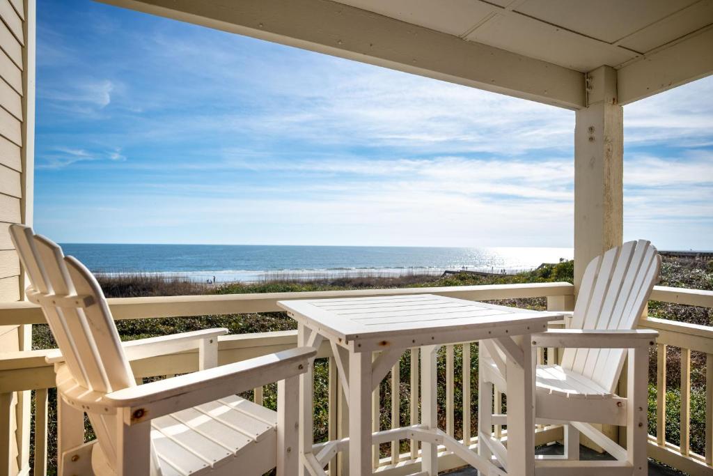 two chairs and a table on a porch with the ocean at Captains Choice by Oak Island Accommodations in Caswell Beach