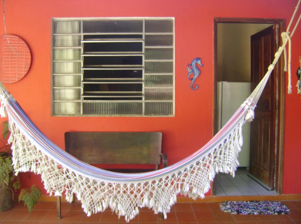 a hammock in a room with a red wall at Suítes Vila do Surf , a original , desde 2010 in Ubatuba