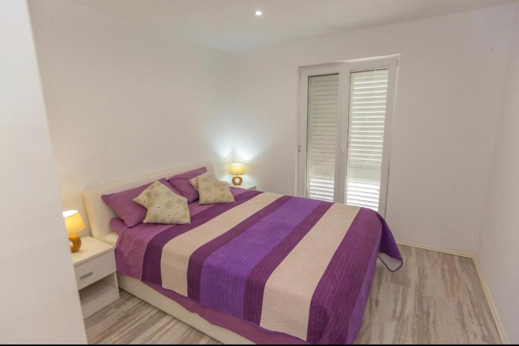 a white bedroom with a purple bed with a window at Apartman Nick in Mlini