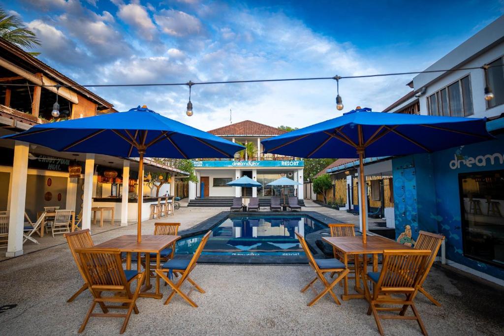 a patio with tables and blue umbrellas next to a pool at Dream Divers Resort in Gili Trawangan