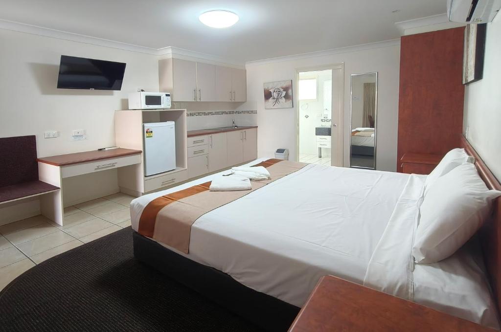 a bedroom with a large white bed and a kitchen at Motel Myall in Dalby