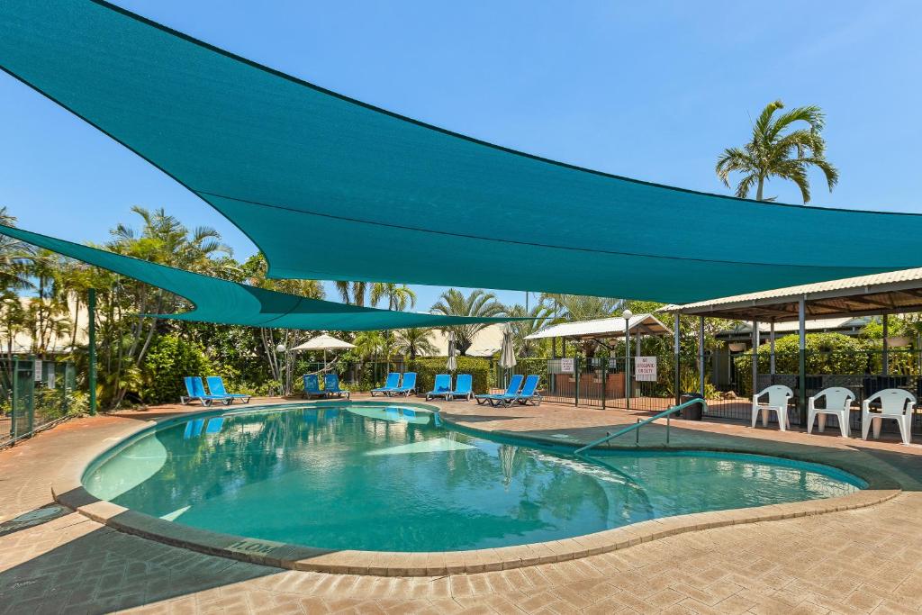 a swimming pool with a blue umbrella over it at Cable Beachside Apartments in Broome