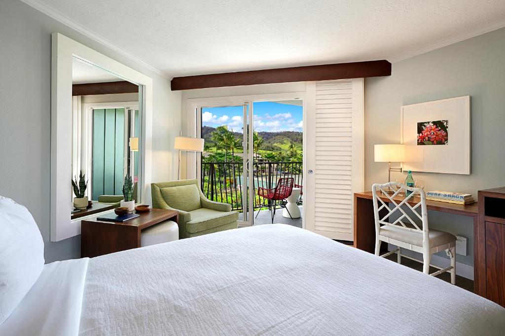 a bedroom with a bed and a desk and a balcony at Kauai Beach Resort in Lihue