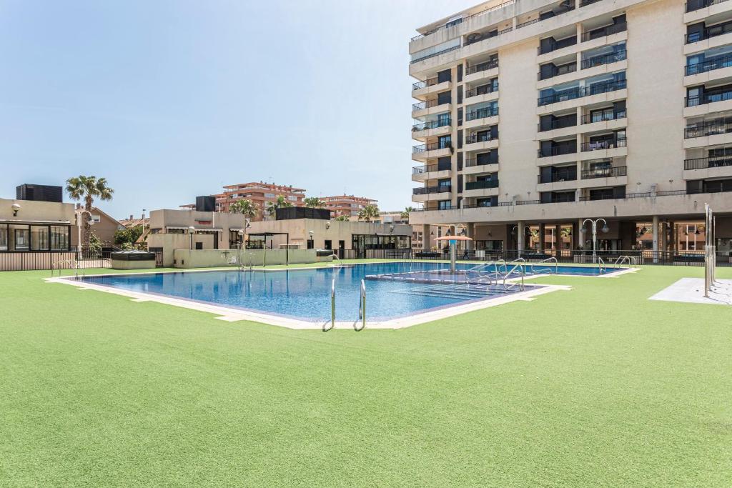 a large swimming pool with green grass and a building at Patacona By The Beach in Valencia