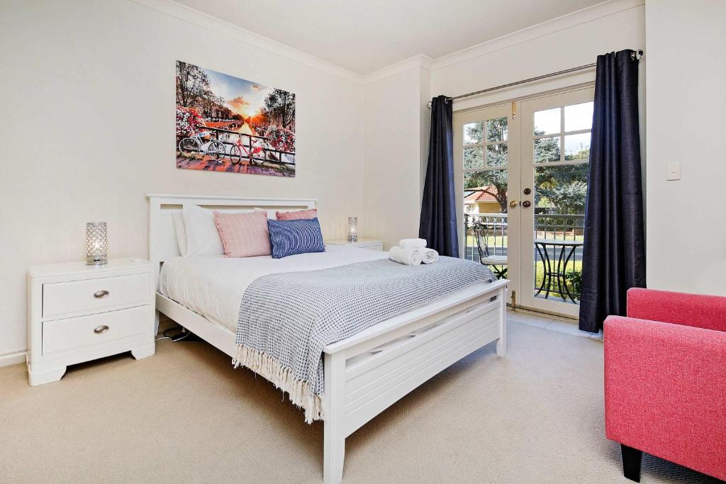 a bedroom with a white bed and a red chair at Archie's Townhouse 4BD 2BT in Glenunga