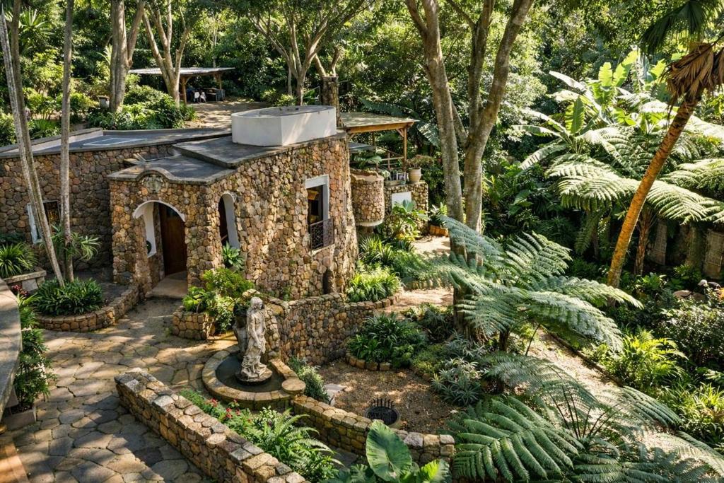 a small stone house in a garden with trees at MacLeod House Guest Cottage in Kloof